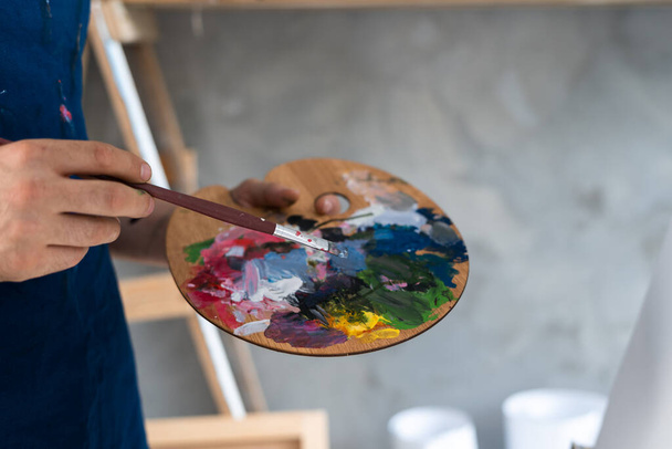 Paleta s barvami zblízka na umělcových rukou drží a míchá různé barvy se štětcem. Kopírovat prostor. - Fotografie, Obrázek