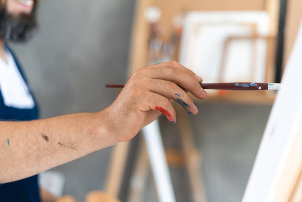 male artist paints a picture with oil brush in hand with palette close-up - Photo, Image