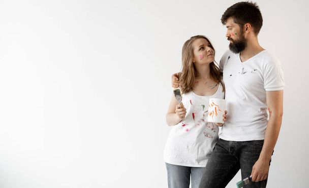 Un homme et une femme en T-shirts sales se tiennent sur un fond blanc et étreignent. Concept de rénovation résidentielle. Baner. Espace de copie. - Photo, image