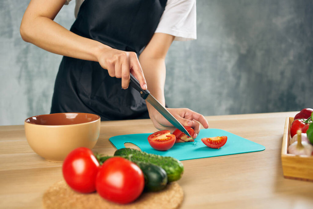 Femme en tablier noir sur la cuisine coupe légumes salade régime - Photo, image