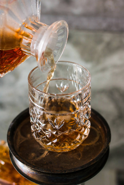 Pouring whiskey in glass with natural ice. Dammed glass with strong alcoholic drink. Vertical photo. - Zdjęcie, obraz