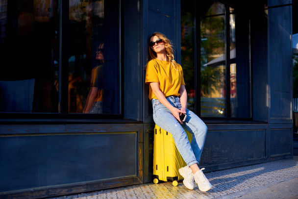 woman tired of walking around city and sit down on yellow suitcase - Foto, imagen