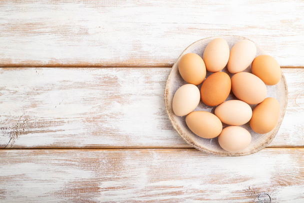 Hromada barevných kuřecích vajec na talíři na bílém dřevěném pozadí. pohled shora, plochá poloha, kopírovací prostor. - Fotografie, Obrázek