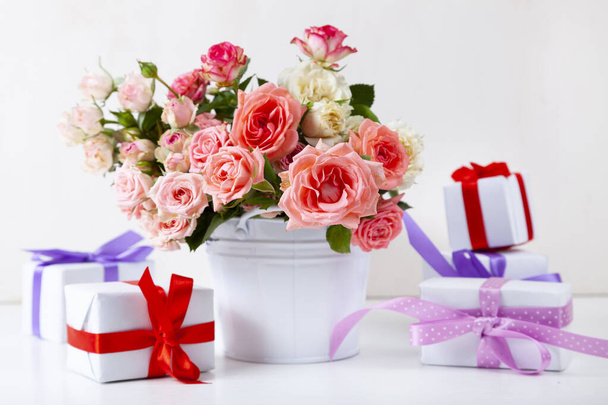 Bouquet of pink roses and boxes with gifts on a light wooden background. - Foto, Imagem