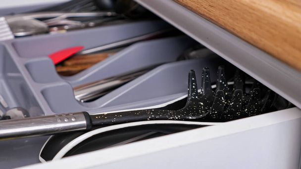 Person closes pull-out kitchen cabinet drawer with utensils - Photo, Image