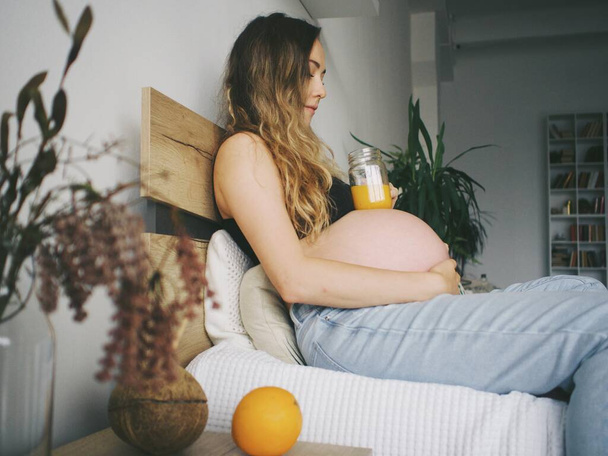 mujer embarazada bebe jugo de naranja recién exprimido, vitaminas para las mujeres embarazadas - Foto, Imagen