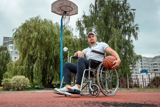 A man in a wheelchair plays basketball on the sports ground. The concept of a disabled person, a fulfilling life, a person with a disability, fitness, activity, cheerfulness. - Foto, Imagem