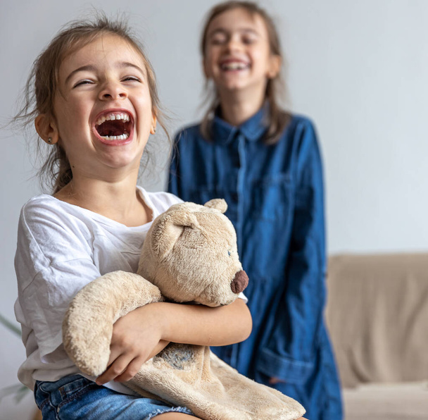 Дві маленькі сестрички граються з плюшевим ведмедем, розважаючись вдома
. - Фото, зображення