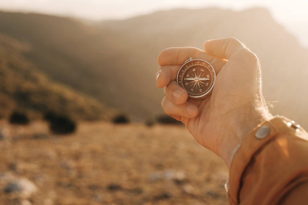 Compass in the hands of a tourist in the mountains during sunset. - Фото, изображение