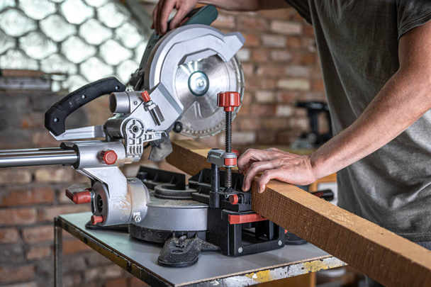 A man with a board and miter saw close up, concept building and repair. - Fotoğraf, Görsel