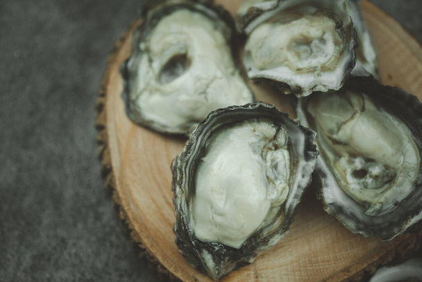 Abrir las ostras frescas en el plato de madera. Disparo desde la parte superior sobre un fondo negro - Foto, imagen