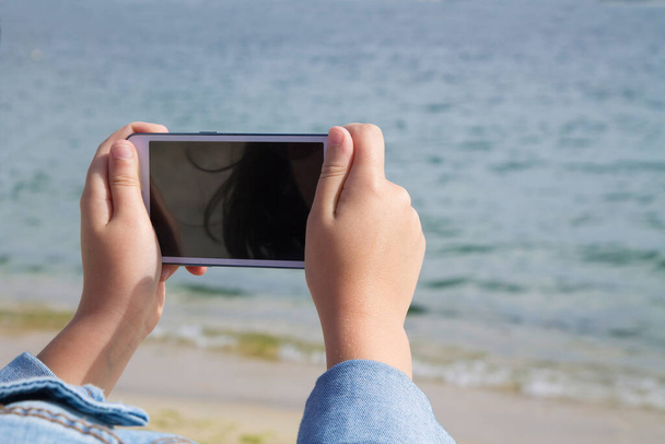 Lány fényképez a mobiltelefon a strand és a tenger - Fotó, kép