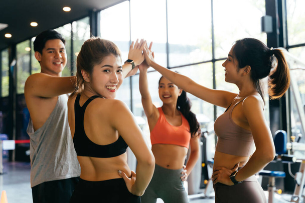Smile man and women making hands together in fitness gym. Group of young people doing high five gesture in gym after workout. Happy successful workout class after training. Teamwork concept. - Фото, изображение