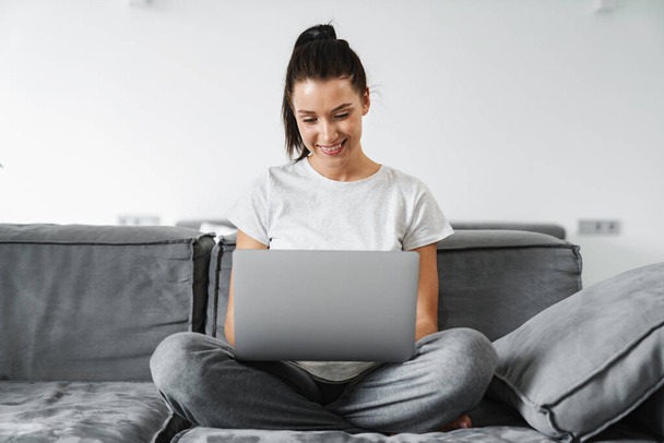 European smiling woman using laptop while sitting on couch at home - Foto, Imagem