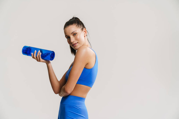 Young white fitness woman in sportswear with ponytail standing over white wall background, holding plastic water bottle - Φωτογραφία, εικόνα