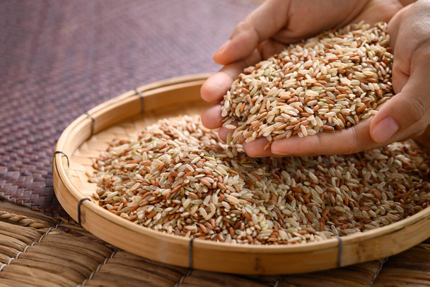 Органічне тайське високогірне каштанове зернятко в бамбуковому кошику з руками (Cargo rice, Loonzain rice або Husked rice), здорова їжа - Фото, зображення