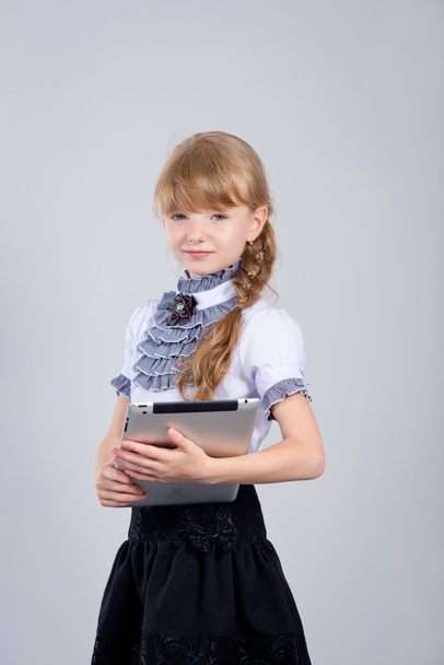 Little schoolgirl smiling while using digital tablet at desk - Zdjęcie, obraz