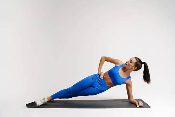 Slim young white sportswoman exercising on a fitness mat in studio, planking - 写真・画像
