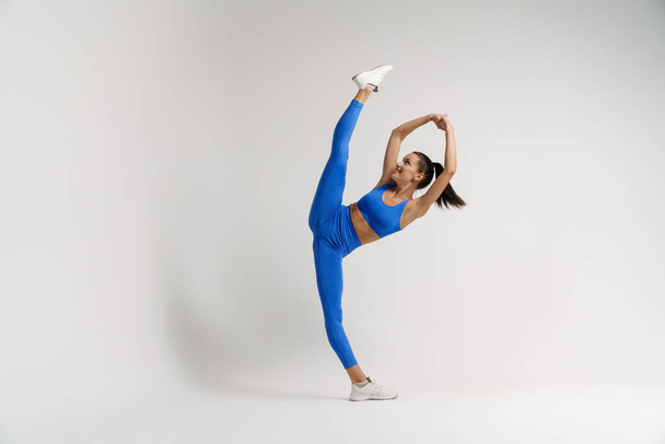 Young flexible white fitness woman in sportswear with ponytail standing in split white wall background - Foto, Imagem
