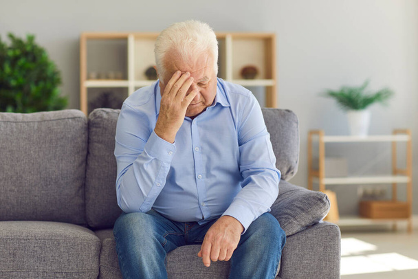 Senior man sitting on couch, grieving over loss of wife, or suffering from bad headache - Фото, зображення