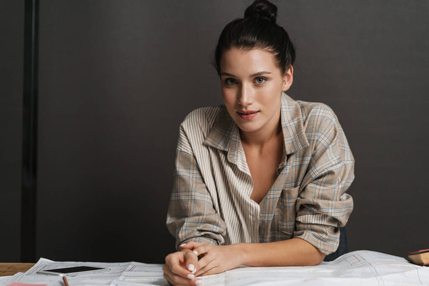 Young smiling casual brunette white woman sitting working at the office desk with paperwork looking at camera - Foto, immagini