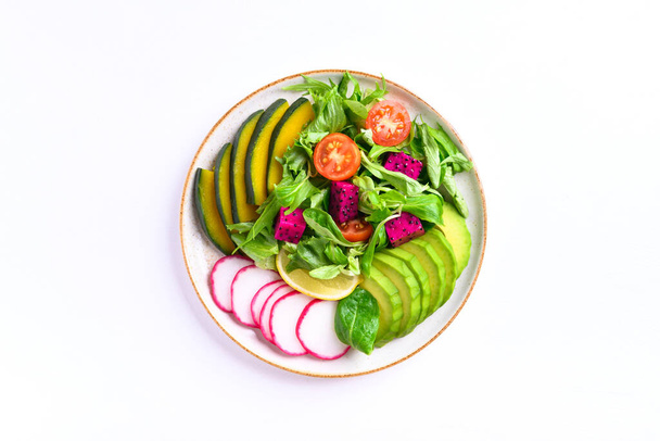 Vegaaninen salaatti hedelmiä ja vihanneksia lautasen avokado, lohikäärme hedelmiä, retiisi, kurpitsa, tomaatti, maissisalaatti, salaatti, mizuna ja sitruuna valkoisella pohjalla. Terveellinen ruoka - Valokuva, kuva