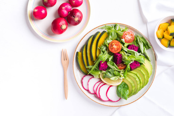 Veganes Salat- und Gemüsegericht mit Avocado, Drachenfrucht, Rettich, Kürbis, Tomate, Maissalat, Salat, Mizuna und Zitrone auf weißem Hintergrund. Gesunde Ernährung - Foto, Bild