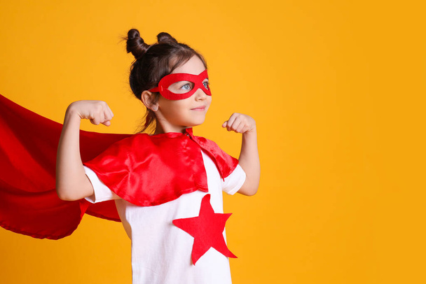 Cute little girl in superhero suit on yellow background. Space for text - Foto, Imagem