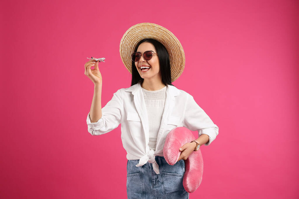 Happy female tourist with toy plane and travel pillow on pink background - 写真・画像