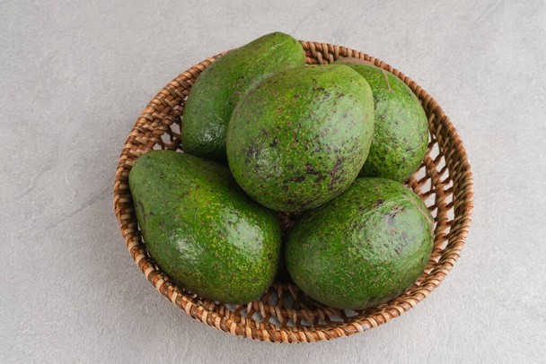 Alpukat or Avocado (Persea americana), ripe and fresh, served in rattan basket on grey background, close up and copy space. - Photo, Image