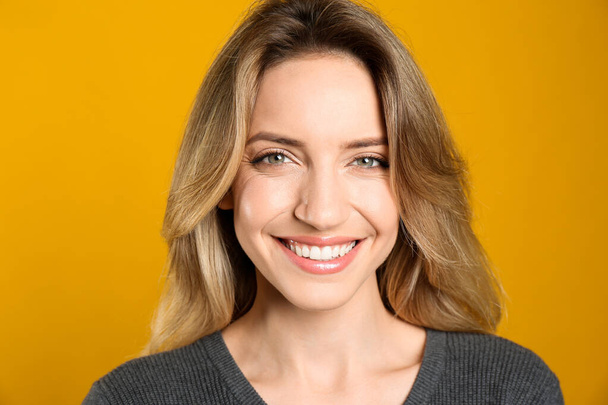 Portrait of happy young woman with beautiful blonde hair and charming smile on yellow background, closeup - Fotó, kép