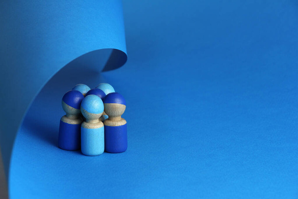 grupo de cinco personas de juguete de madera azul están cubiertas con una hoja de papel azul, concepto de trabajo en equipo o seguridad integrada, fondo azul con espacio de copia - Foto, imagen