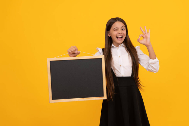 niño sorprendido en uniforme mantenga la pizarra escolar para el espacio de copia que muestra gesto ok, publicidad - Foto, Imagen
