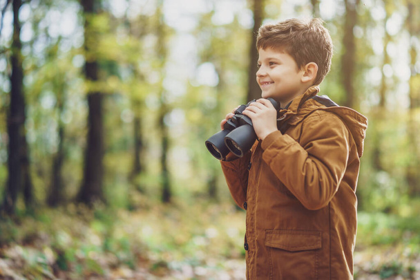Portrait of boy who is hiking in nature with binoculars in autumn. - Photo, Image
