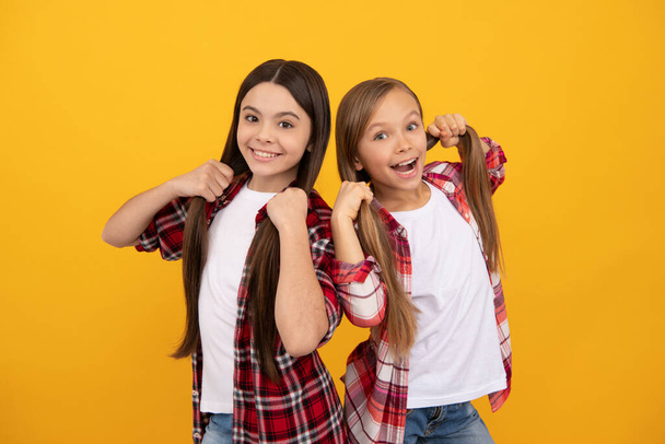 heureux enfants en casual à carreaux chemise tenir les cheveux longs et raides sur fond jaune, cheveux - Photo, image