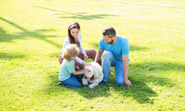 padre madre e hijo en la hierba verde del parque. familia amigable con mascota. - Foto, Imagen