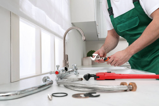 Professional plumber fixing water tap in kitchen, closeup - Foto, Bild