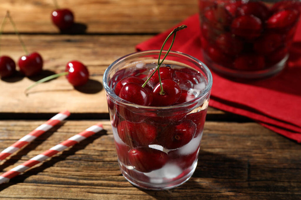 Sweet red cherries with ice cubes in glass on wooden table - Фото, зображення