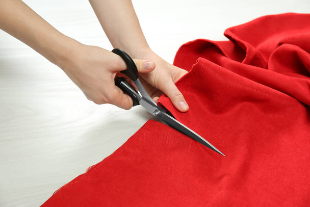Seamstress cutting red fabric with scissors at workplace, closeup - Fotó, kép