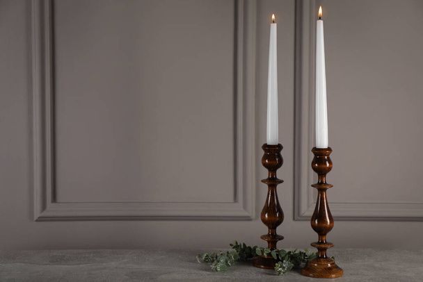 Elegant candlesticks with burning candles and eucalyptus on grey table. Space for text - Zdjęcie, obraz