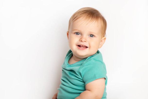 Baby kindje jongen in groen t-shirt lacht blij te kijken naar de camera geïsoleerd op een witte achtergrond. Concept kinderopvang en opvoeding. - Foto, afbeelding