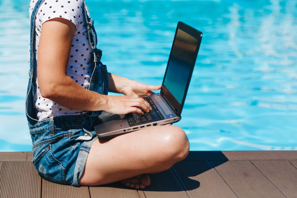 Woman working on her laptop computer sitting at poolside. ummer day near the beach resort, freelance concept - Photo, image