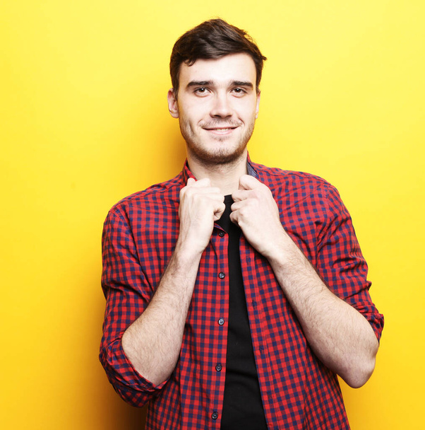 Portrait of handsome unshaven young man wearing red plaid shirt posing on camera isolated over yellow background - Fotografie, Obrázek