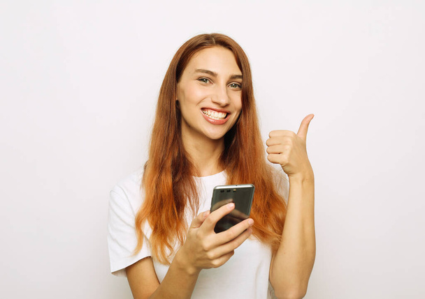 Photo of cheerful beautiful young red-haired woman chatting by mobile phone and show thumbs up - Foto, immagini