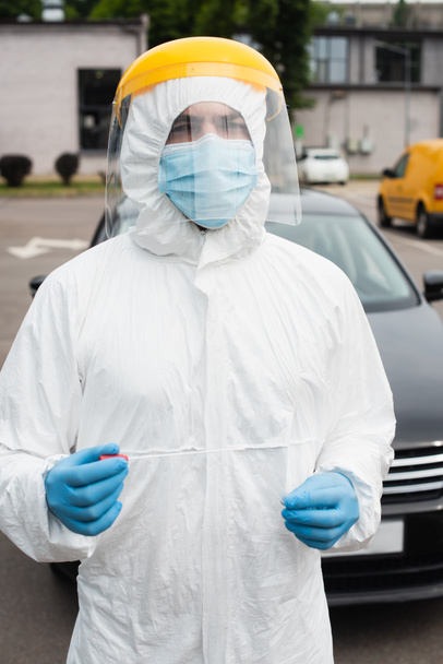 Medical worker in protective visor holding pcr test near blurred car outdoors  - Foto, imagen