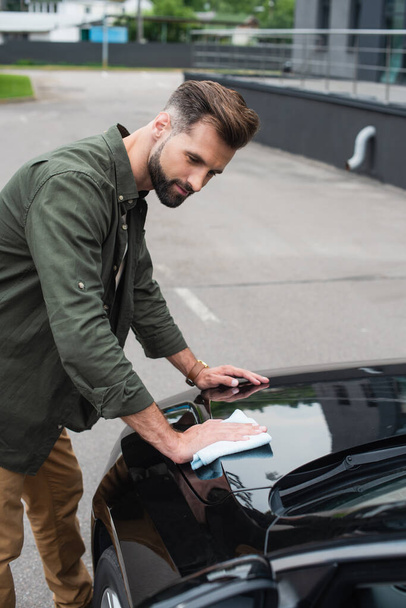 Young man in casual clothes wiping car outdoors  - Foto, Imagem