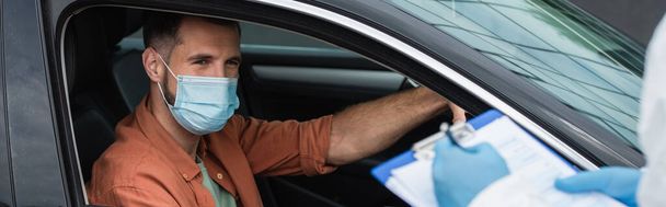 Kierowca w masce patrząc na niewyraźny pracownik medyczny pisząc na tablicy, baner  - Zdjęcie, obraz
