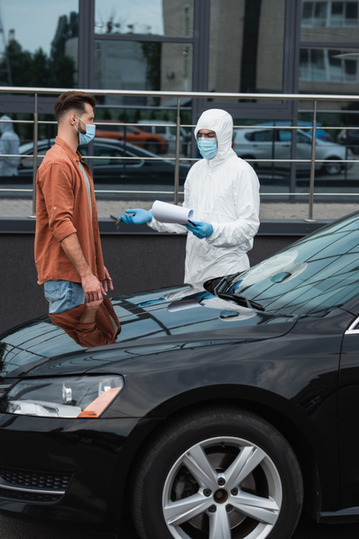 Chauffeur masqué debout près d'un travailleur médical avec presse-papiers pointant la main à l'extérieur  - Photo, image