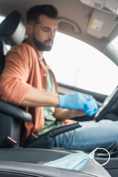 Medical mask in car near blurred driver in latex gloves - Foto, afbeelding
