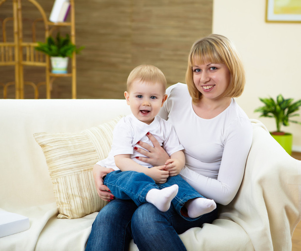 Little boy and his young mother together at home sitting on the sofa - Фото, изображение